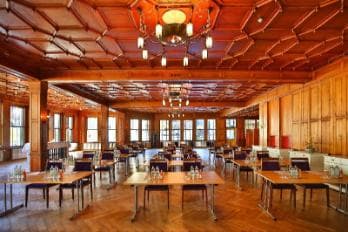 Large wood-paneled room with coffered ceiling, chandelier, and many tables set for an event.