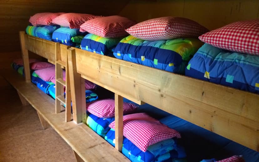 Bunk beds with colorful bedding and red gingham pillows inside a wooden mountain hut or hostel.