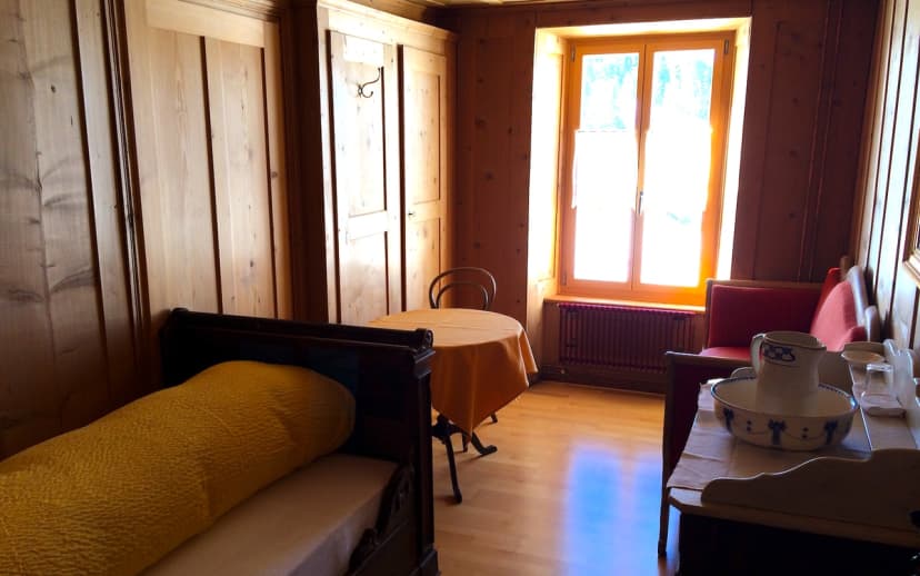 Hotel room with wood paneling, bright window, bed with yellow bolster, and wash basin set.