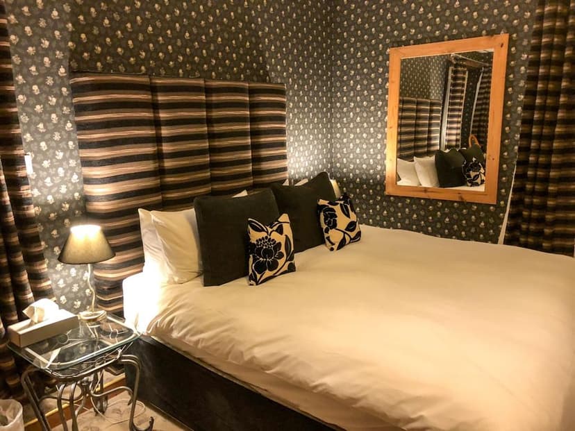 Bedroom with patterned wallpaper, striped headboard, white duvet, and wooden framed mirror.
