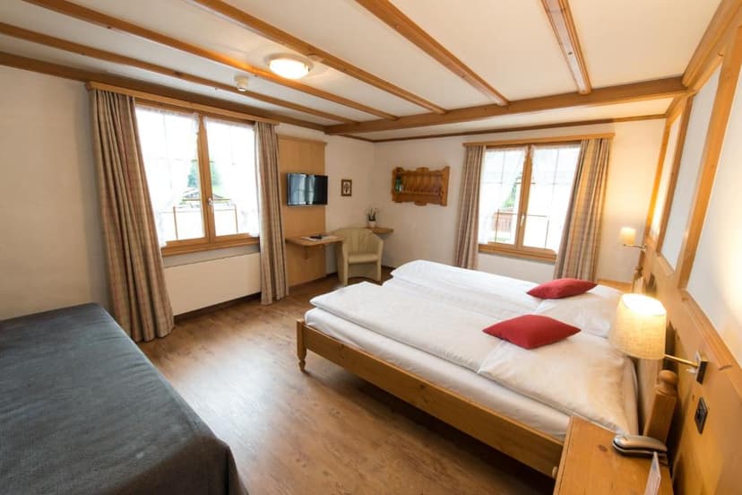 Twin beds with white linens and red pillows in a room with wood beams at Sporthotel Victoria Gstaad.
