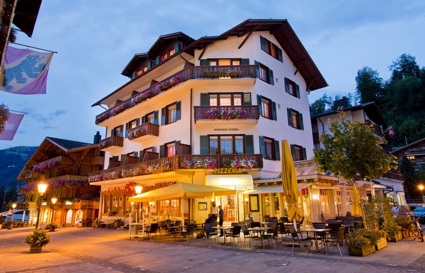 Sport Hotel Victoria in Gstaad with illuminated restaurant patio at dusk, alpine setting.