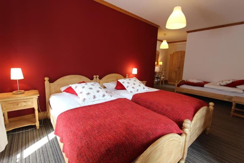 Twin wooden beds with red bedding against a deep red wall in a hotel room