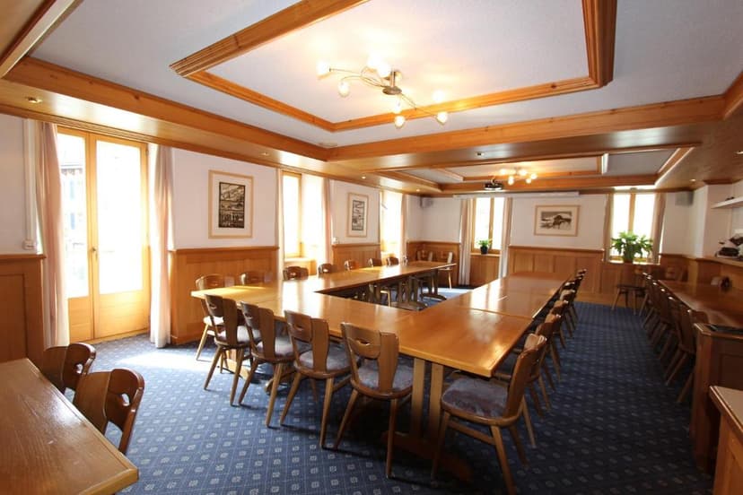 Conference room with U-shaped wooden table, wooden paneling, and blue patterned carpet.