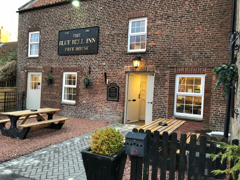 The Blue Bell Inn free house exterior with brick wall, picnic tables, and open doorway