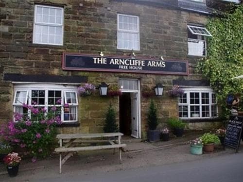 The Arncliffe Arms Free House pub entrance with stone facade, flowers, and picnic bench.