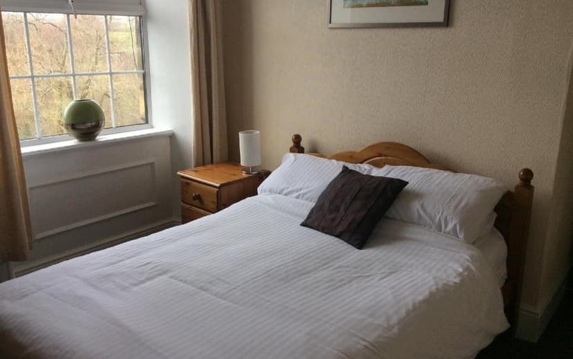 Bedroom with double bed, white linens, wooden headboard, and view of trees outside.