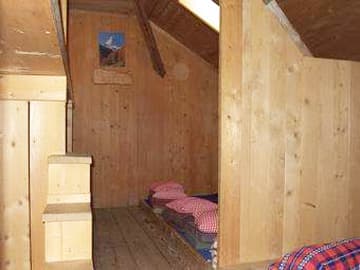 Simple wooden interior of a mountain hut or attic room with beds and a small picture on the wall.