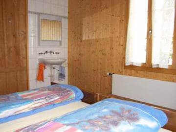 Twin beds with blue duvets in a wood-paneled room with a sink area.