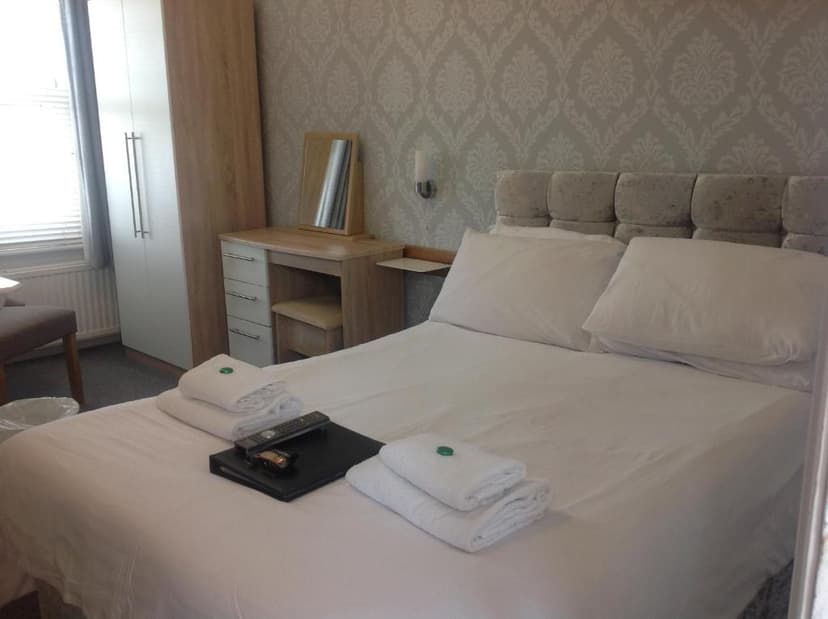 Bedroom in Grosvenor Hotel with white linens, patterned wallpaper, and wooden furniture.