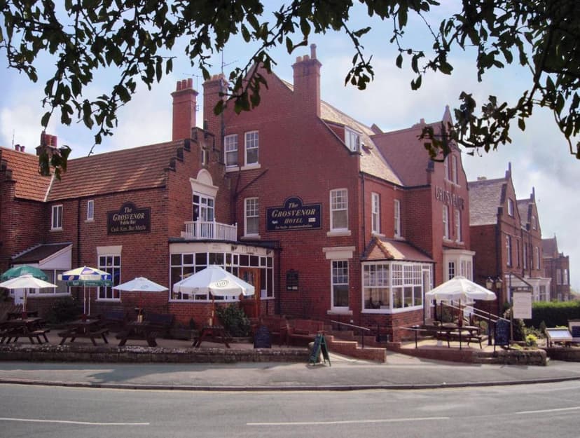 The Grosvenor Hotel pub with outdoor seating under umbrellas, framed by tree branches.