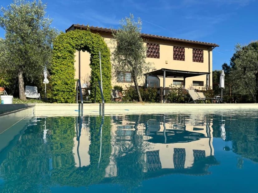 Agriturismo building reflected in swimming pool with ivy archway and olive trees