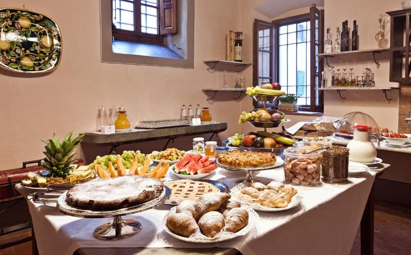 Buffet breakfast spread with cakes, fruit, croissants, and juice in a room with wooden windows.