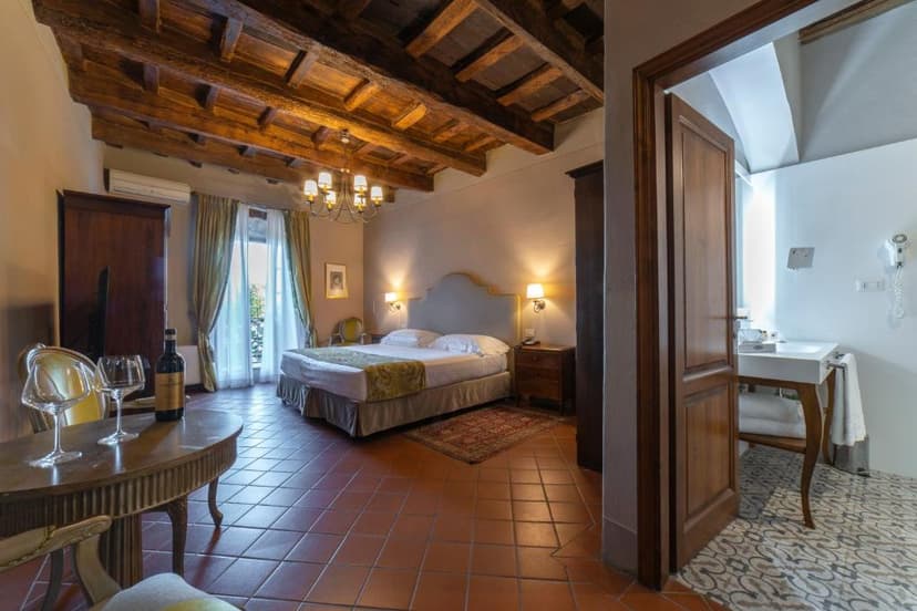 Hotel bedroom with wood beam ceiling, terracotta floor, and view into a white bathroom.