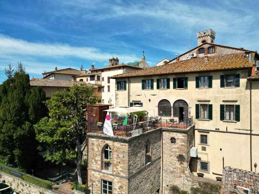 Rooftop terrace dining area on stone building in historic Italian town under blue sky.
