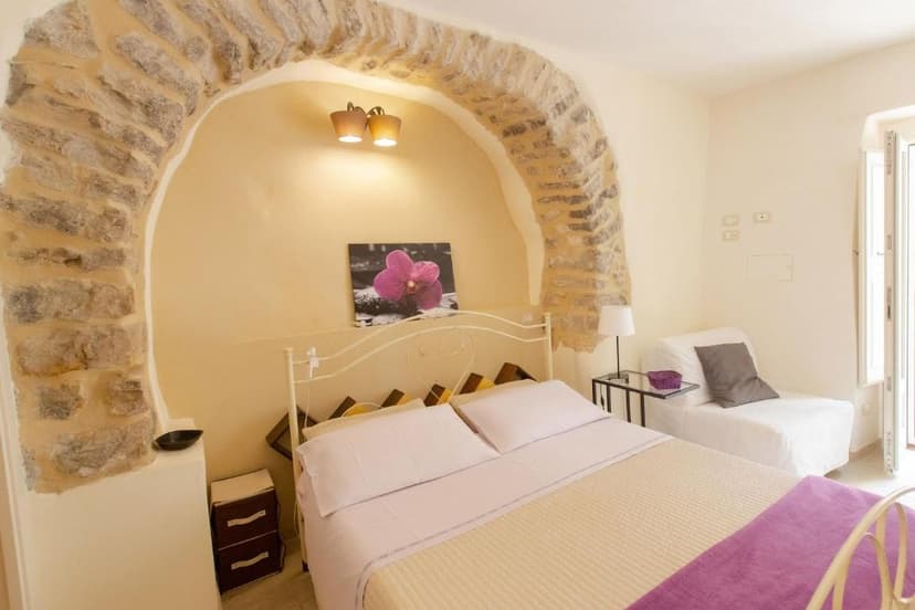 Bedroom with white metal bed, stone archway, and purple orchid artwork