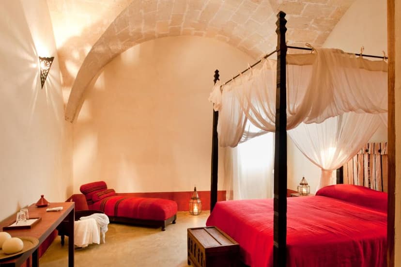 Bedroom with four-poster bed, red linens, vaulted stone ceiling, and Moroccan-style lantern.
