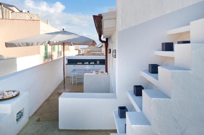 Rooftop terrace with white built-in stairs, outdoor kitchen area, and umbrella near the sea in Favignana.