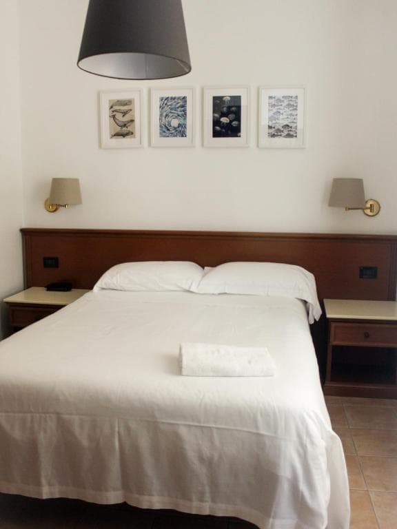 Double bed with white linens, dark wood headboard, and four framed marine art prints.