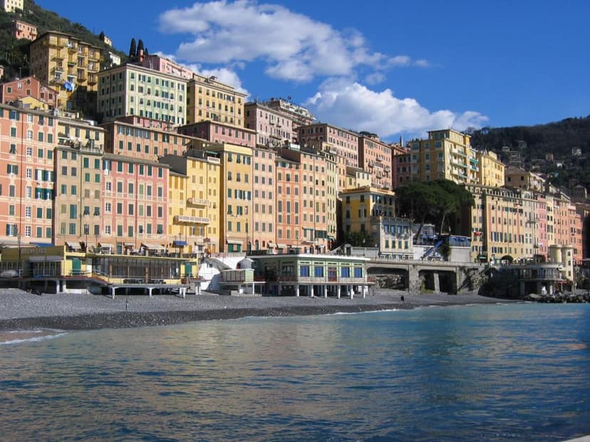 Colorful buildings rise up a hillside above a pebbled beach and blue sea in Camogli, Italy.