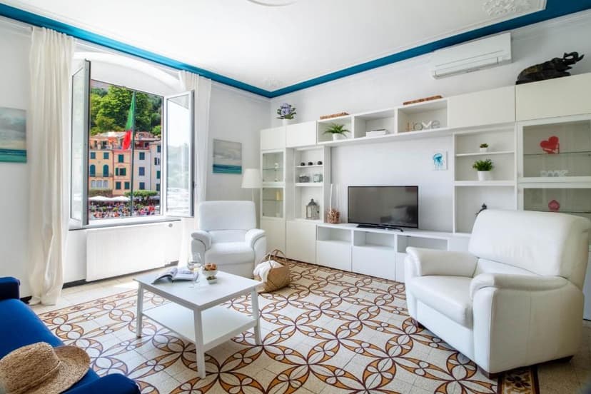 Living room with white furniture overlooking colorful buildings and a hillside view of Portofino.