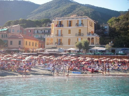 Crowded beach with umbrellas and buildings below green mountains, viewed from the sea at Monterosso.
