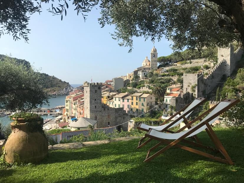 Two deck chairs on a lawn overlooking the colorful coastal village of Portovenere, Italy.