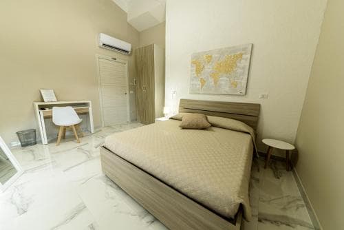 Bedroom in Corleone Guesthouse with beige bedding, modern desk, and world map art