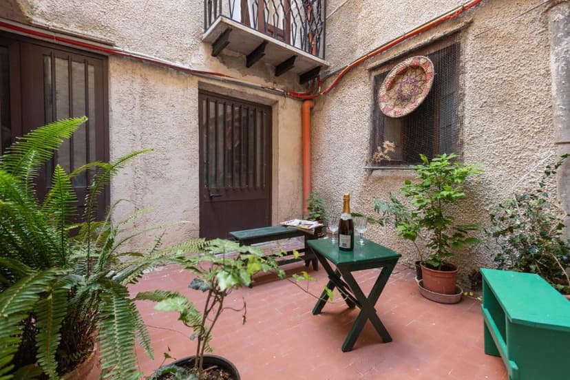 Small enclosed courtyard with potted ferns, green tables, and a bottle of champagne.