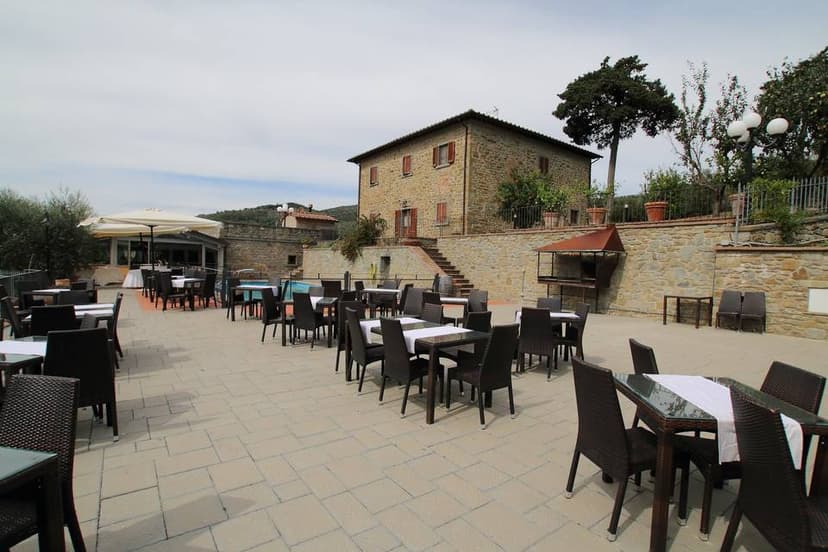 Outdoor dining terrace with wicker tables and chairs overlooking a stone building and hills.