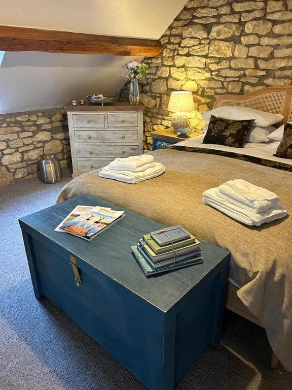 Bedroom with stone walls, wicker headboard, and blue storage chest at foot of bed.