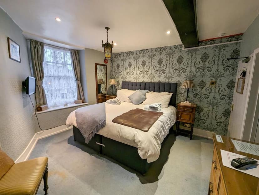 Bedroom in Crown and Trumpet Inn with patterned wallpaper, large bed, and window.