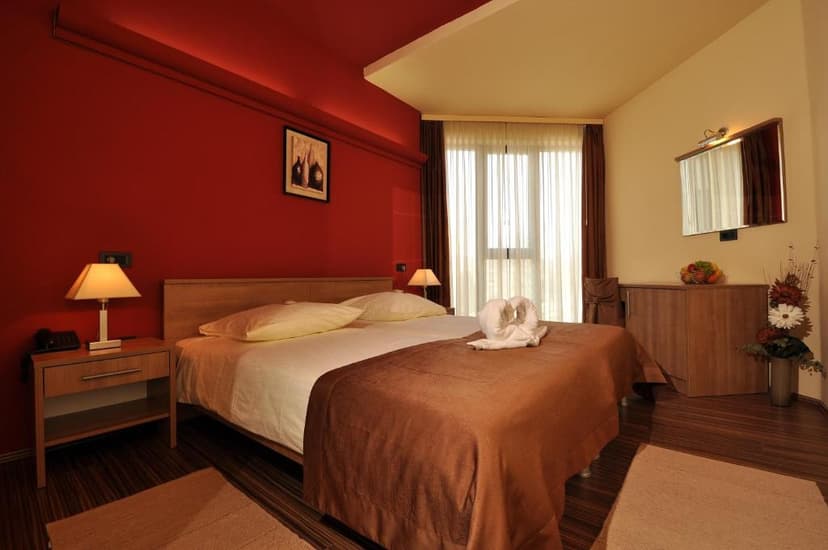 Hotel room with red accent wall, wooden furniture, and a bed with towel swans.