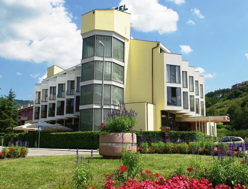 Modern hotel building with yellow accents, large windows, and flower beds under a blue sky.