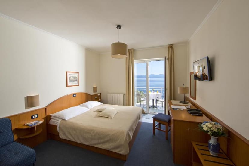 Hotel room with double bed, balcony view of sea and mountains, and desk area.