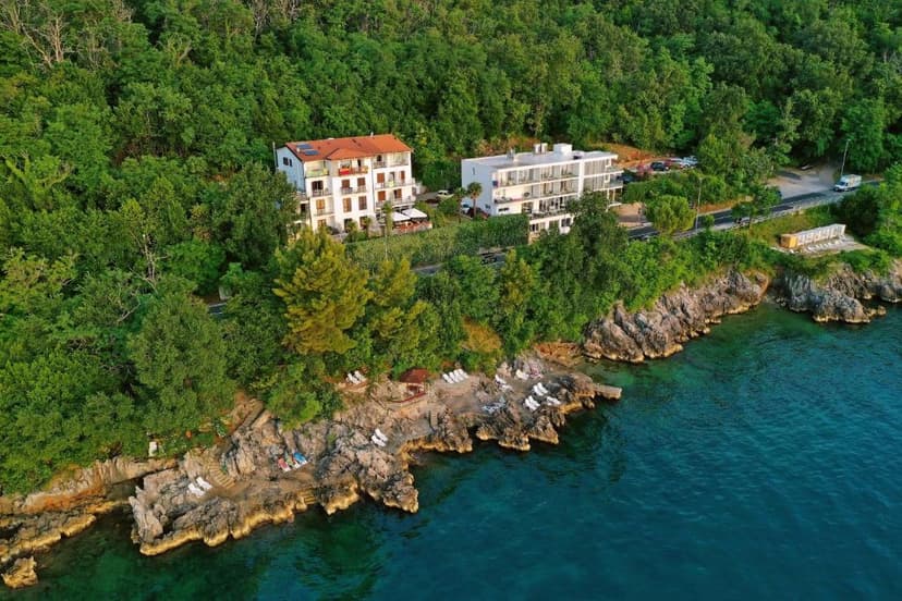 Hotels nestled in dense green forest above rocky coastline and clear blue water