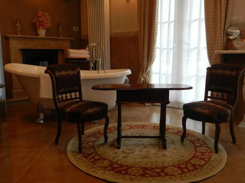 Luxurious bathroom with clawfoot tub, antique table, two chairs, and fireplace.