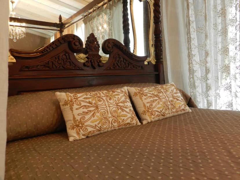 Four-poster bed with carved dark wood headboard, embroidered pillows, and sheer curtains