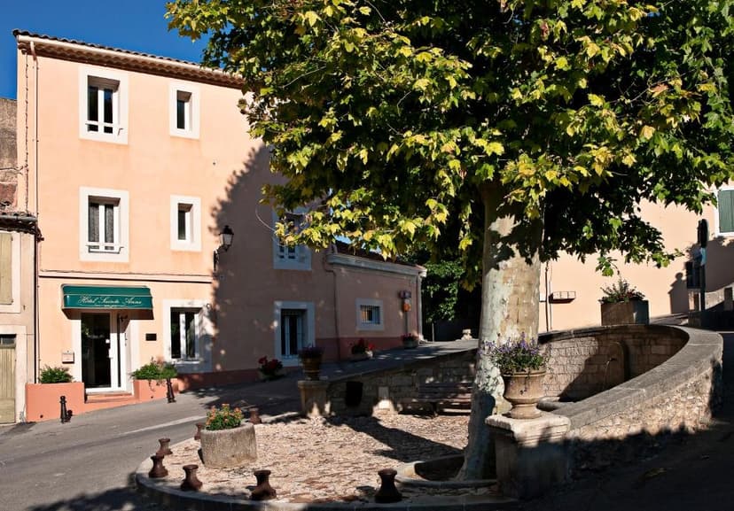 Hotel Sainte Anne entrance on a sunny street corner with a large tree and stone fountain.