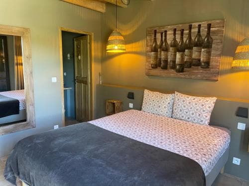 Bedroom with large bed, wine bottle art, and woven hanging lamps, Luberon style.
