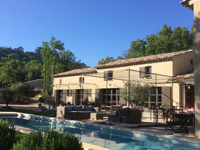 Stone villa with outdoor seating and swimming pool near wooded hills in Luberon.
