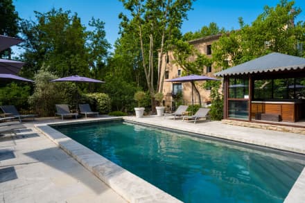 Swimming pool with lounge chairs and purple umbrellas next to a historic building, Hôtel du Poète.