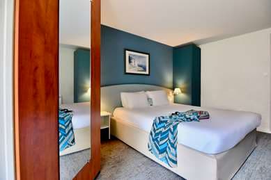 Hotel Kyriad bedroom with white bedding, blue accent wall, and mirrored closet door reflection.