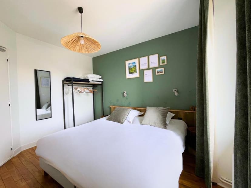 Bedroom with white bedding, green accent wall, and woven pendant light at Hôtel-Restaurant La Maison.