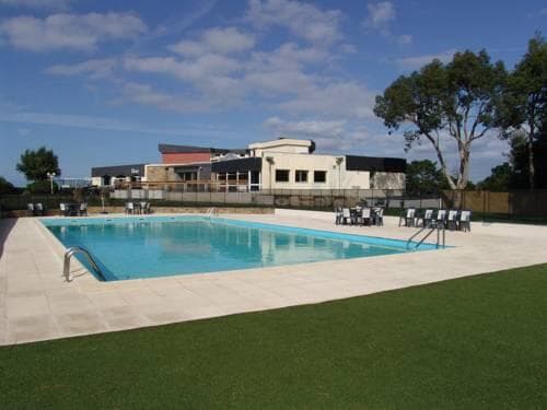 Outdoor swimming pool with sun loungers and hotel building in background at Brit Hotel Golf Hotel Saint Samson.