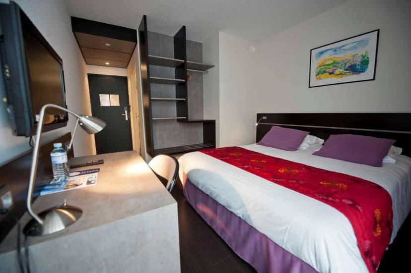 Modern hotel room with double bed, desk, TV, and open shelving at Brit Hotel Golf Hotel Saint Samson.