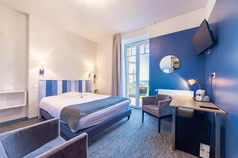 Hotel room with blue accent wall, bed, and view of the sea through glass doors in Ploumanac'h.