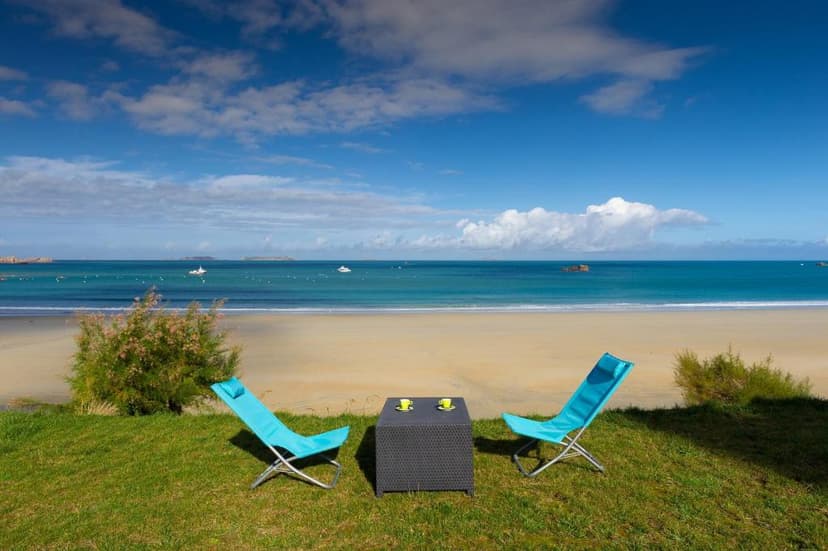 Two blue lounge chairs and table on grass overlooking Ploumanac'h beach and blue sea.
