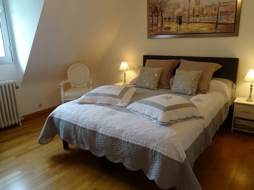 Bedroom in attic space with white and grey quilted bedding, lamps, and artwork.