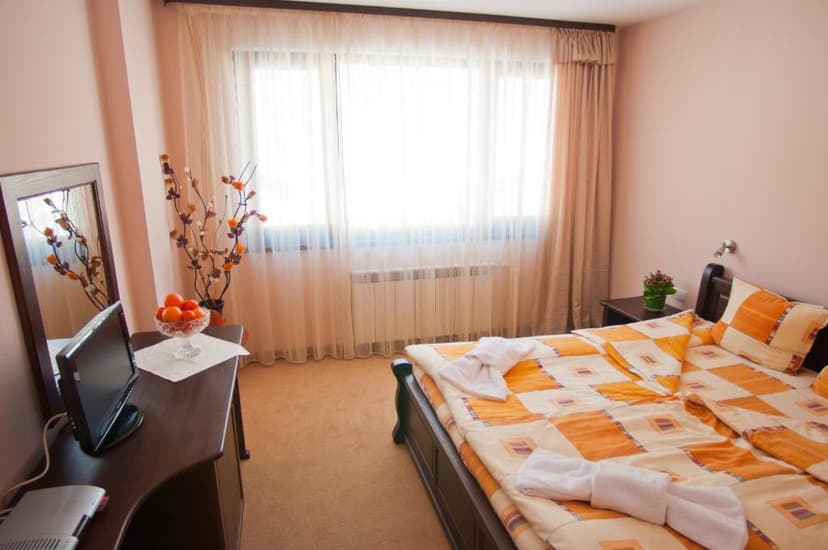 Hotel room with orange patterned bedding, dark wood furniture, and a large window with sheer curtains.